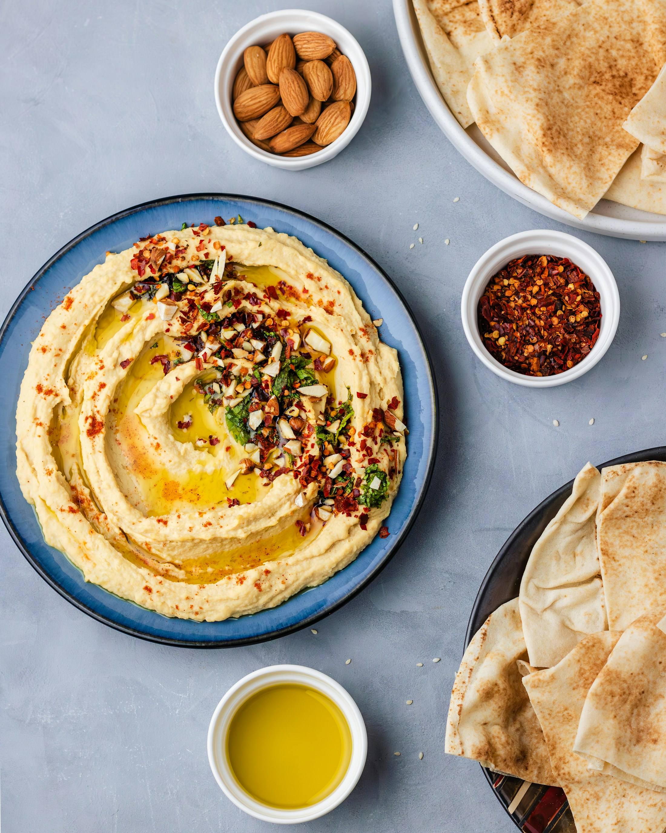 Hummus met olijfolie en kruiden, naast pitabrood en een schaaltje olijfolie.