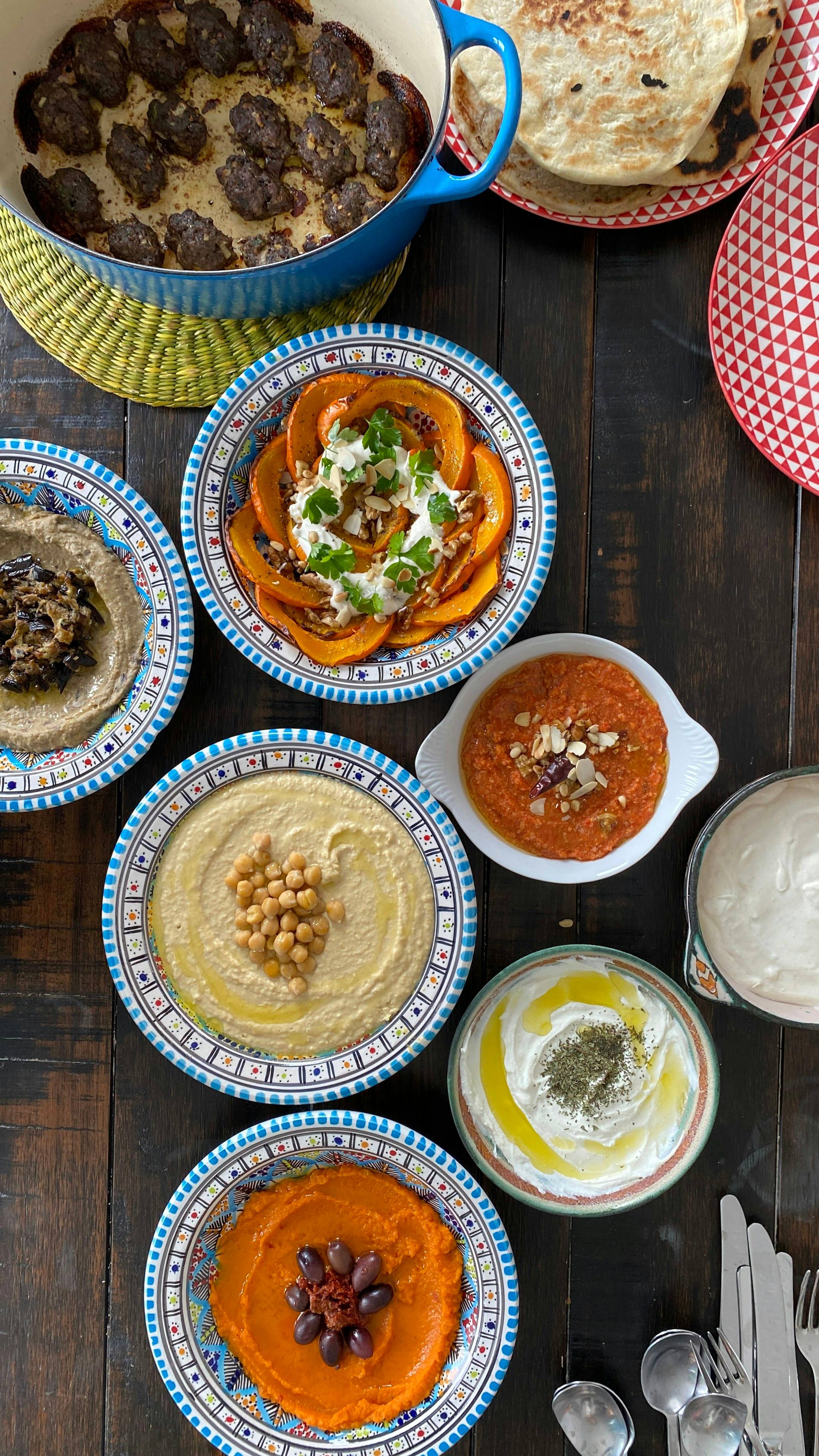 Een gedekte tafel met hummus, linzensoep, yoghurt met olijfolie en andere schaaltjes in beschilderd aardewerk.