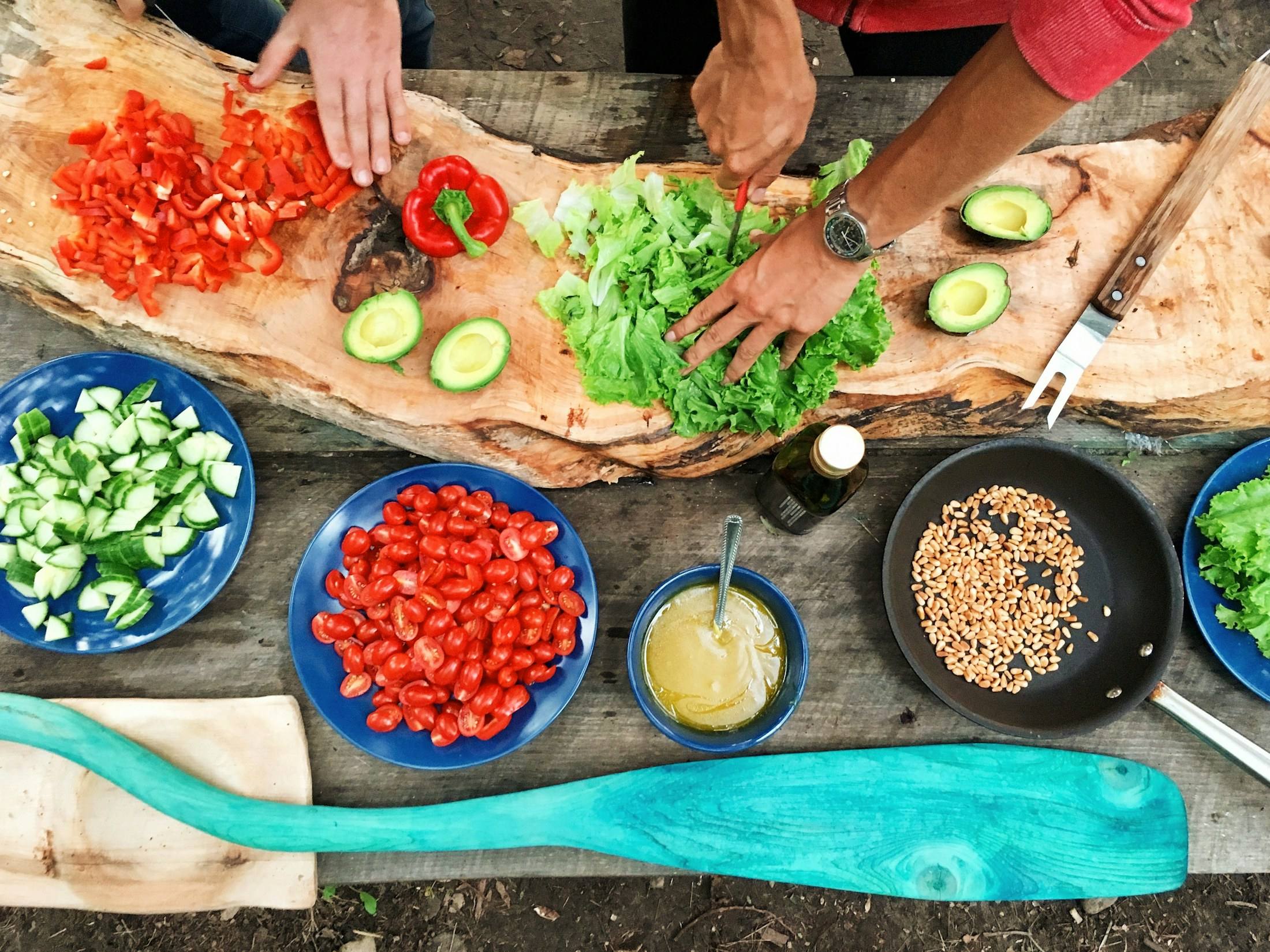 Samen koken: handen snijden groenten naast schaaltjes met tomaat, komkommer en kruiden.